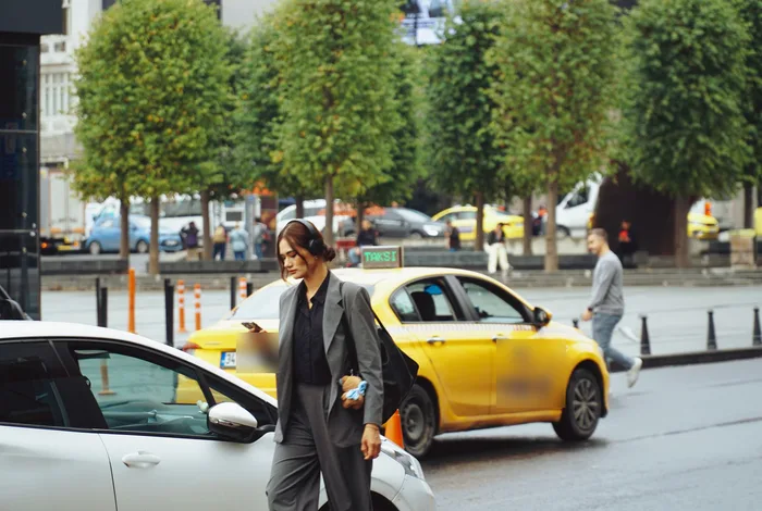 Telefonuna bakarak yürüyen kadın ve arkasında sarı taksi